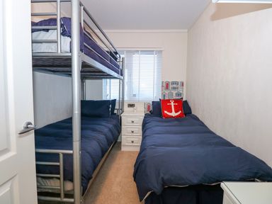 A bedroom with a bunk bed, a single bed, a nightstand, and a window with blinds at Un Diwrnod The Warren T22 The Warren near Abersoch