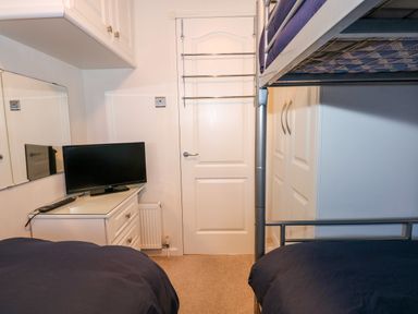 A small bedroom with bunk beds a television on a dresser a mirror and a door with a towel rack at Un Diwrnod The Warren T22 The Warren near Abersoch