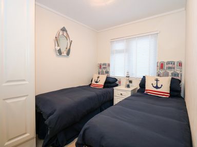 A bedroom with two single beds with navy bedding a nightstand between the beds and a window with blinds at Un Diwrnod One Day The Warren T22 The Warren near Abersoch