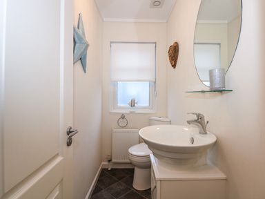 A small bathroom with a toilet sink a round mirror and a window at Un Diwrnod The Warren T22 The Warren near Abersoch