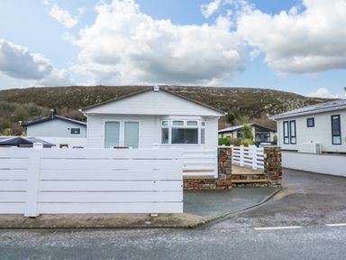 A white single-story house with a white fence and stone pillars in front at The Warren near Abersoch