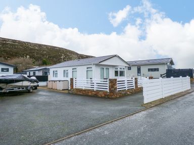 A white single-story house with a fenced porch and boat parked on driveway at Un Diwrnod The Warren T22 The Warren near Abersoch