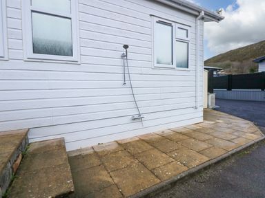An outdoor shower attached to a white building with two frosted windows and stone steps leading to a paved area at Un Diwrnod The Warren T22 The Warren near Abersoch