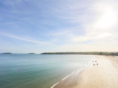 A beach with calm sea and people walking along the shore at The Warren near Abersoch