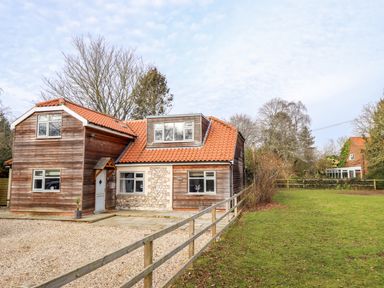 A wooden house with a tiled roof next to a gravel driveway and a fenced grass area at Natterjacks in Syderstone