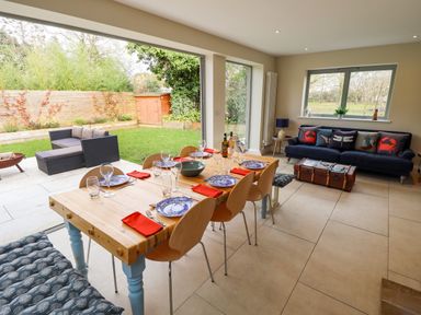 A dining area with a wooden table set for six and a living room with a blue sofa and cushions at Natterjacks in Syderstone