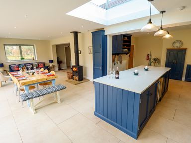 A kitchen and dining area with a wooden table set for meals a wood stove and blue cabinets at Natterjacks in Syderstone