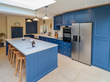 A kitchen with blue cabinets a large island with stools and a stainless steel refrigerator at Natterjacks in Syderstone