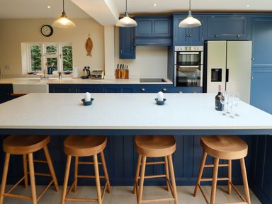 A kitchen with blue cabinets a white countertop a kitchen island with wooden stools candles a bottle and glasses at Natterjacks in Syderstone