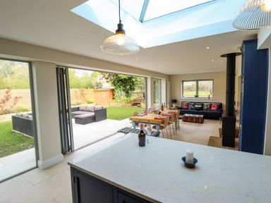 An open plan kitchen and dining area with a large skylight folding glass doors to a garden and a blue sofa with cushions at Natterjacks in Syderstone