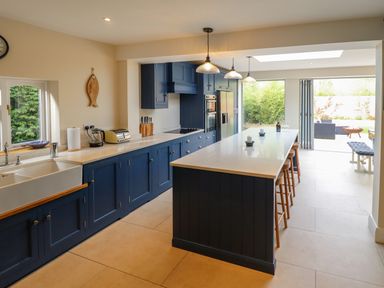 A kitchen with blue cabinets a long island with stools and sliding glass doors opening to a garden at Natterjacks in Syderstone