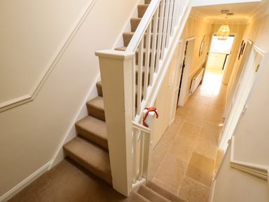 A staircase with beige carpet leading down to a tiled hallway with doors along the sides and a hanging light at Natterjacks in Syderstone