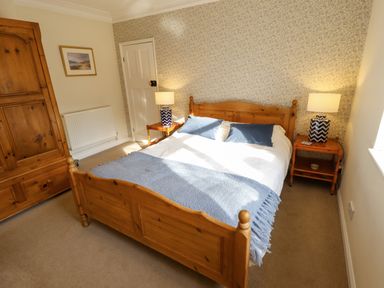 A bedroom with a wooden double bed blue pillows and blankets bedside tables with lamps a wooden wardrobe carpeted floor and patterned wallpaper at Natterjacks in Syderstone