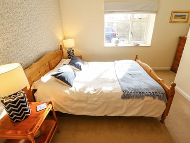 A bedroom with a wooden double bed with blue pillows and a blue throw next to a window and wooden bedside tables with lamps at Natterjacks in Syderstone