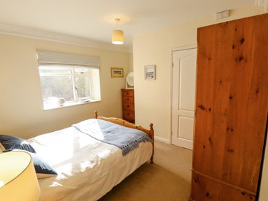 A bedroom with a wooden bed a wooden wardrobe a chest of drawers and a window at Natterjacks in Syderstone
