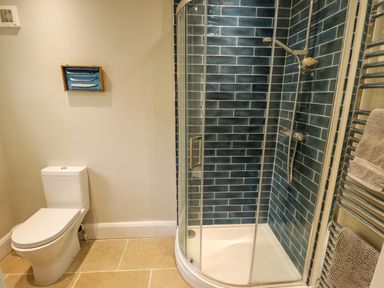 A bathroom with a toilet a glass shower enclosure with blue tiled walls and a towel rack with towels at Natterjacks in Syderstone