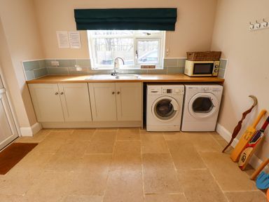 A utility room with a sink washing machine dryer microwave and sports equipment at Natterjacks in Syderstone