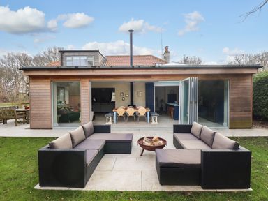 An outdoor seating area with black sofas and a fire pit in front of a wooden house with large glass doors at Natterjacks in Syderstone