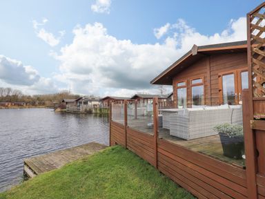 A lakefront lodge with a wooden deck and outdoor seating near Carnforth