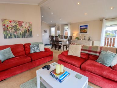 A living room with two red sofas and a white coffee table by a dining area at Otters Reach near Carnforth