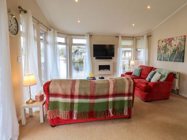 A living room with red sofas and a wall-mounted TV at Otters Reach near Carnforth