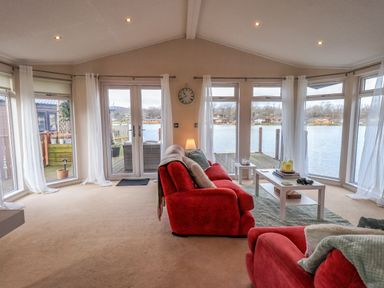 A living room with red sofas a coffee table and large windows overlooking a lake at Otters Reach near Carnforth