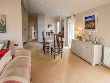 A dining area with a table and chairs next to a sideboard with decorations at Otters Reach near Carnforth