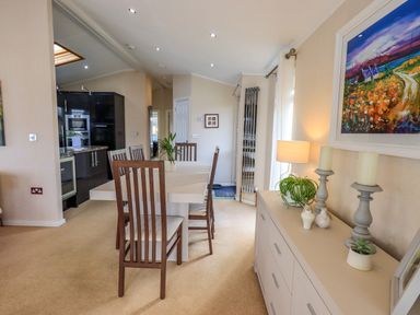 A dining area with a table and chairs next to a sideboard with candles and plants at Otters Reach near Carnforth