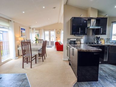 An open plan kitchen and dining area with dark cabinets and a dining table with chairs at Otters Reach near Carnforth