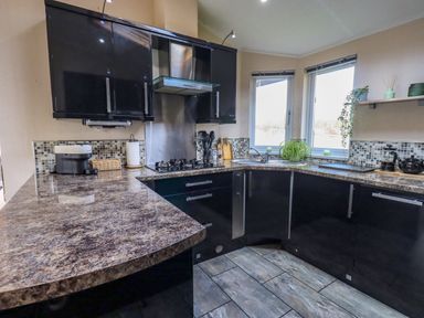 A kitchen with black cabinets a marble countertop a gas stove a sink under windows and kitchen appliances at Otters Reach near Carnforth