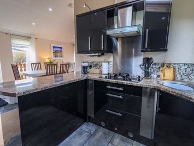 A kitchen with black cabinets a dining table with chairs and a window at Otters Reach near Carnforth