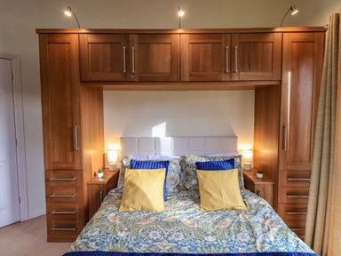 A bedroom with a bed featuring patterned bedding and pillows surrounded by built-in wooden cabinets at Otters Reach near Carnforth