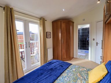 A bedroom with a bed blue and yellow bedding wooden wardrobe and glass double doors leading to a balcony at Otters Reach near Carnforth