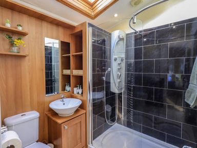 A bathroom with a toilet sink mirror shelves and a shower with black tile walls at Otters Reach near Carnforth