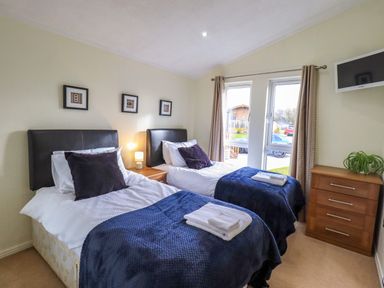 A bedroom with two single beds bedside table and chest of drawers at Otters Reach near Carnforth