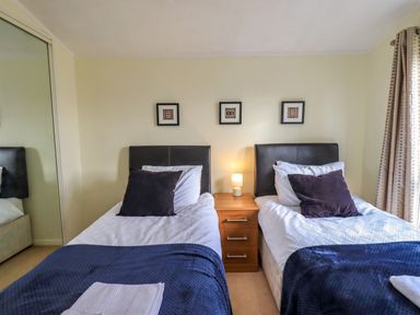 A bedroom with two single beds with dark headboards a nightstand in between and framed pictures on the wall at Otters Reach near Carnforth