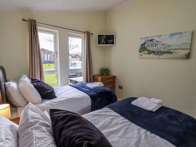 A bedroom with two single beds a wall-mounted TV and a painting at Otters Reach near Carnforth