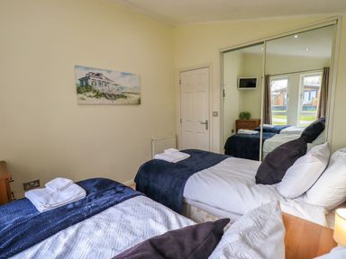 A bedroom with two beds a wooden nightstand a wall painting and mirrored closet doors at Otters Reach near Carnforth