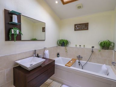 A bathroom with a white bathtub a wooden bath tray a white sink with dark wood vanity and plants at Otters Reach near Carnforth