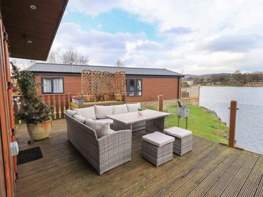 An outdoor deck with a wicker outdoor sofa set and table near a lake at Otters Reach near Carnforth