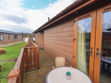 A deck with a table and chair outside wooden cabin near water at Otters Reach near Carnforth