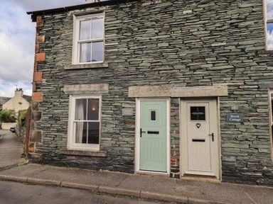 Stone exterior wall with two windows and two doors of cottages named Capella Cottage and Brock Cottage in Keswick