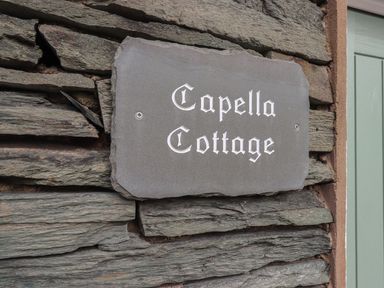 A stone wall with a sign reading Capella Cottage next to a green door at Capella Cottage in Keswick