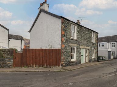 A stone and white house with two colored doors on a street with a wooden fence at Capella Cottage in Keswick