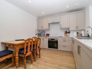 A kitchen with cabinets, oven, sink, and dining table at Capella Cottage in Keswick