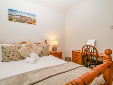A bedroom with a bed, nightstand, chair, and a photograph at Capella Cottage in Keswick