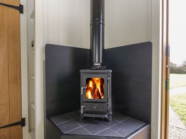 A wood burning stove with fire inside in a corner with black paneling at Blackthorn South Leigh near Witney