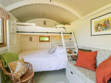 A bedroom with bunk beds a wicker chair with a cushion a small sofa with orange pillows and a painting on the wall at Blackthorn in South Leigh near Witney