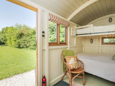 A small bedroom with bunk beds a chair with cushions and a green blanket by an open door showing a grassy area outside at Blackthorn in South Leigh near Witney