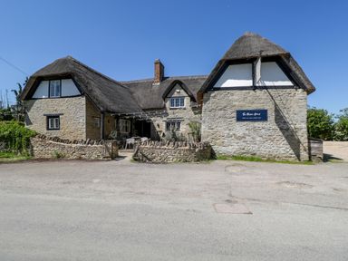 A thatched roof stone building with outdoor seating and a sign that reads The Mason Arms